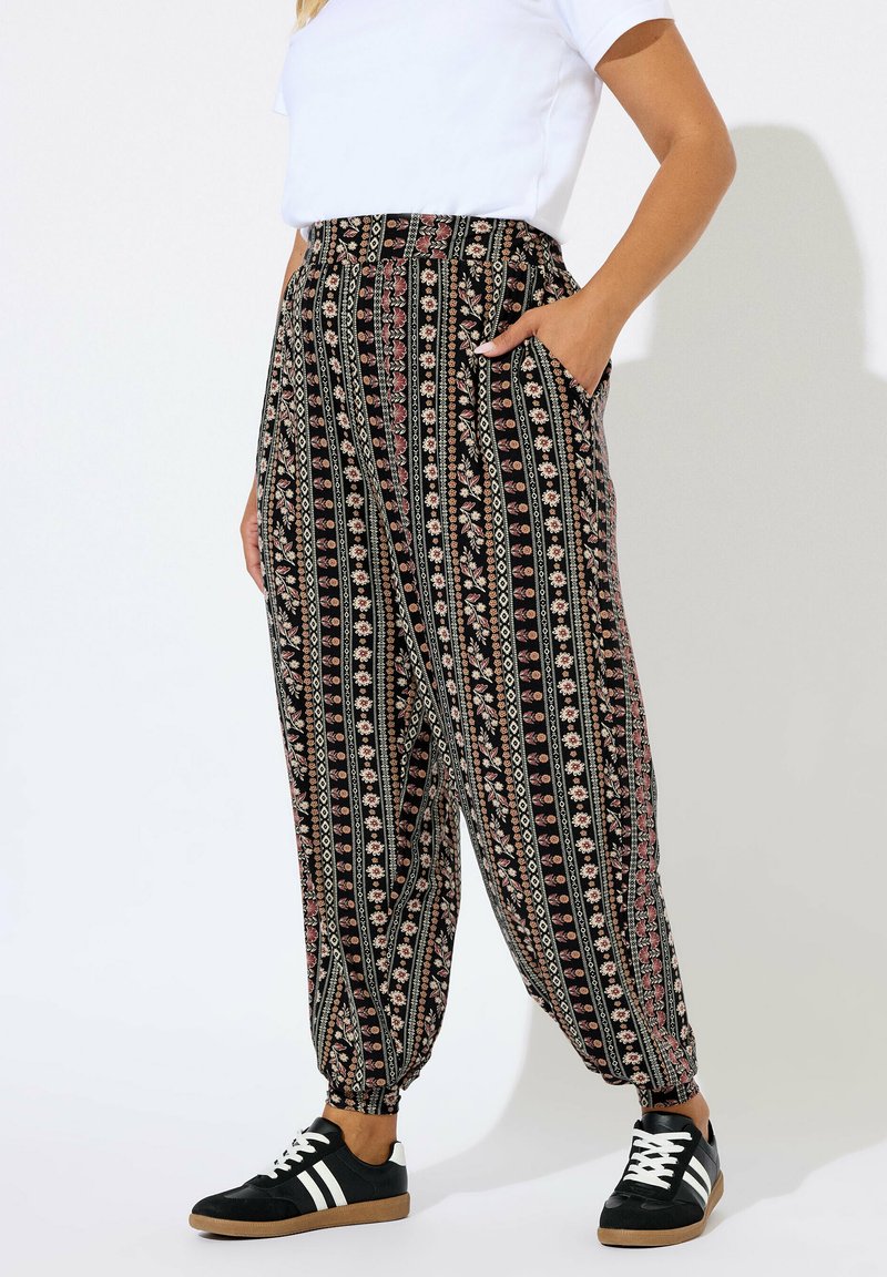 Persoon in hoge taille bloemenpatroon broek met elastische boorden, een witte top met korte mouwen, en zwarte sneakers met witte strepen.