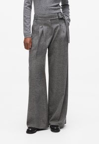 Graue Wollhosen mit weitem Bein, Falten und einem taillierten Bund, der einen schwarzen Ledergürtel und silberne Schnallenakzente aufweist.