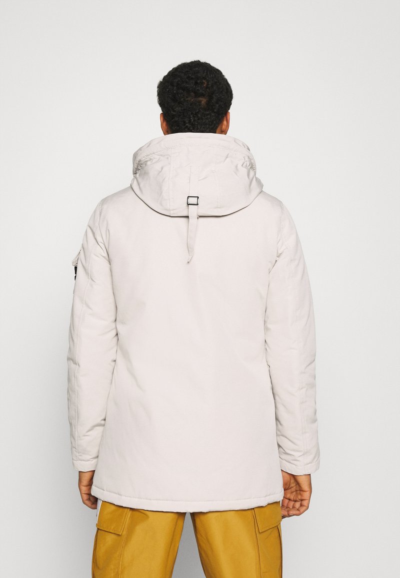 Parka gris clair avec capuche, dotée d'un cordon de serrage et d'une sangle réglable, texture lisse et coupe plus longue.