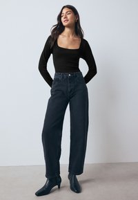 Top negro de manga larga con escote cuadrado combinado con vaqueros de mezclilla oscura de talle alto. La modelo lleva botas negras de tacón hasta el tobillo.