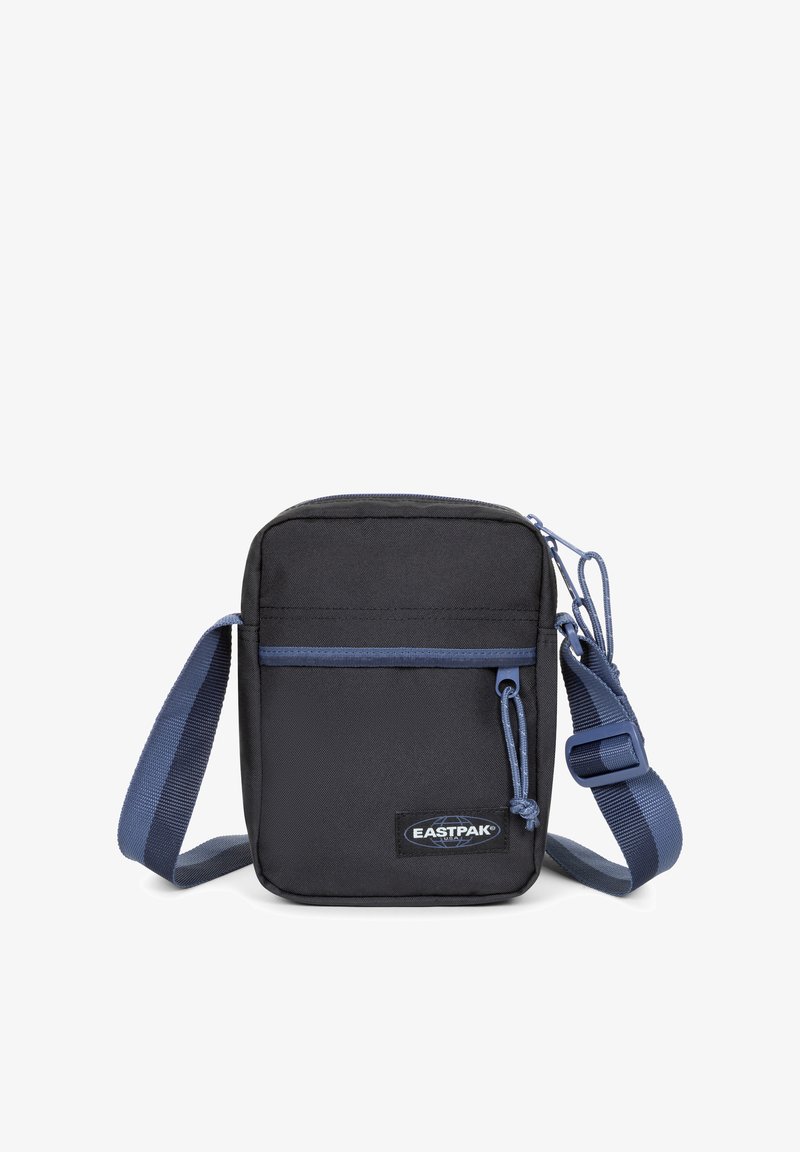 Černá látková krosbody taška s přední kapsou na zip, modrými detaily, nastavitelným popruhem a nášivkou s logem Eastpak. Obdélníkový tvar.