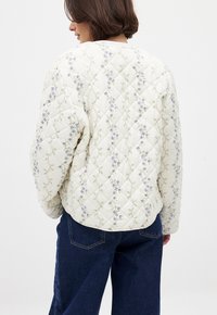 Veste matelassée en tissu crème, ornée d'une délicate broderie florale en violet et vert. Coupe décontractée avec un ourlet arrondi.