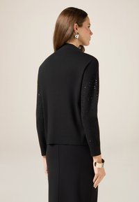 Czarny dzianinowy kardigan z okrągłym dekoltem i rękawami o długości 3/4, zdobiony dekoracyjnymi kryształkami na rękawach. Gładka faktura.