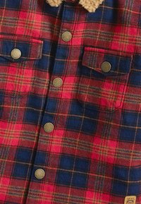 Rot und marineblau kariertes Flanellhemd mit braunen Knöpfen und zwei Brusttaschen mit knöpfbaren Klappen.