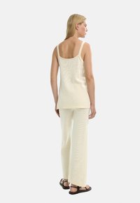 Jasno beżowy dzianinowy top na cienkich ramiączkach, zestawiony z pasującymi szerokimi dzianinowymi spodniami. Tekstura jest miękka z delikatnym wzorem w całej odzieży.