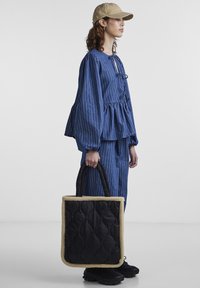 Μπλε ριγέ τοπ με πλούσιο τελείωμα και φουσκωτά μανίκια, συνδυασμένο με ταιριαστά παντελόνια. Μαύρη τσάντα χειρός με καπιτονέ υφή και κρέμα περιθώριο. Καπέλο και χοντρές μαύρες υποδήσεις.