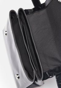 Black patent leather handbag with a glossy finish. Features two main compartments lined with black fabric and silver snap closure.