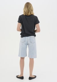 Černé bavlněné tričko, světlé modré denimové šortky a černé baleríny. Tričko má ohrnuté rukávy; šortky jsou po kolena s třepeným lemem.