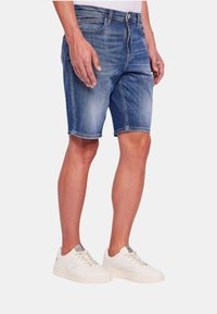 Shorts in denim blu medio, con un classico design a cinque tasche, leggera scoloritura e taglio dritto. Abbinati a sneakers bianche.