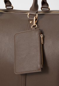 Brown leather handbag with gold hardware, featuring a textured surface, dual handles, and a detachable cardholder with a zipper.