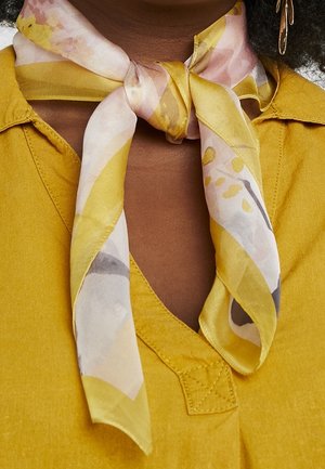 Écharpe en soie jaune avec des motifs abstraits roses, gris et blancs, nouée autour du cou, associée à un haut jaune à encolure en V.