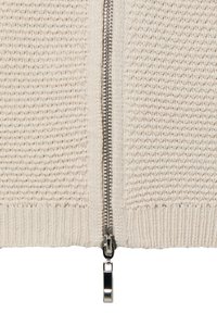 Cardigan tricoté de couleur crème, avec une fermeture éclair centrale, un ourlet côtelé et un tissu texturé présentant un motif subtil. Fermeture éclair en métal argenté.