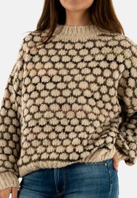 Maglione oversize lavorato a maglia color crema con pois multicolore a trama. Presenta un collo e polsini a coste. Abbinato a jeans in denim blu.