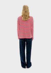 Rood en wit gestreept lang mouwbedrijf met een ontspannen pasvorm, gecombineerd met blauwe wijde jeans. Soepele stof, gedetailleerde stiksels zichtbaar.