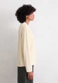Langsleeve, lichtgele top van zacht stof, met een rechte snit en een eenvoudige kraag, gecombineerd met donkere, gestreepte broek.