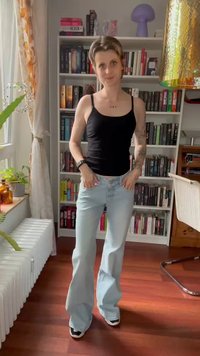 Lyseblå piggede jeans med en falmet finish, parret med en tætsiddende sort tanktop. Teksturerede træhylder fyldt med bøger i baggrunden.