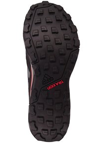 Black rubber shoe sole with deep treads and textured pattern; features "TRAXION" and "adidas" logos in red and white accents.
