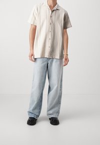 Košile s krátkým rukávem, světlé barvy, texturovaná, s vertikálními pruhy, kombinovaná s volnými světle modrými džíny a černými robustními botami.