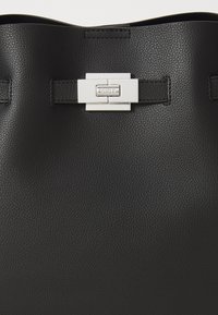Sac fourre-tout en cuir noir avec une texture lisse et un fermoir en métal argenté portant le logo de la marque gravé. Design simple et moderne.
