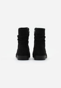 Botas de tobillo de ante negro con un diseño arrugado, cremallera trasera y un tacón bajo apilado, que presentan una textura suave y punta redondeada.