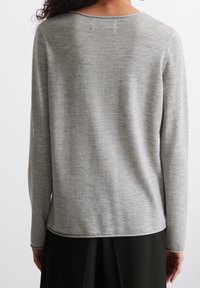 Pull gris à manches longues avec un col arrondi, une texture douce et un tricot lisse. Le dos présente un ourlet légèrement incurvé et un minimum de détails.