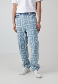 Jeans de un azul claro con un patrón de logotipos repetidos en un tono más oscuro de azul. Corte holgado con diseño estándar de cinco bolsillos y cierre de botón plateado.