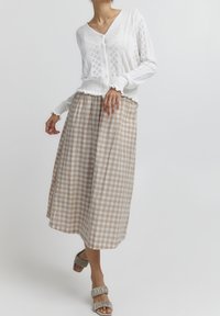 Valkoinen neulecardigan, jossa on v-pääntie ja napit, yhdistettynä polvimittaiseen beigeen ja valkoiseen ruutuhameeseen. Teksturoitu kangas ja pehmeät röyhelöt.