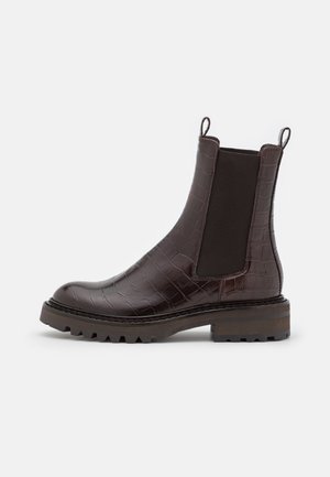 Bottines en cuir crocodile synthétique marron avec panneaux latéraux élastiques, bout rond et semelle en caoutchouc texturée présentant un design à crampons.