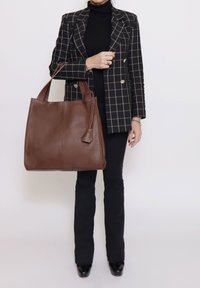 Borsa tote in pelle marrone con superficie strutturata, doppie maniglie e targhetta staccabile. Forma rettangolare oversize, design liscio e strutturato.