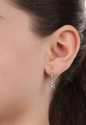 Orecchini a cerchio in argento con un design floreale, arricchiti da gemme verdi e accenti trasparenti, che pendono sotto il lobo dell'orecchio.
