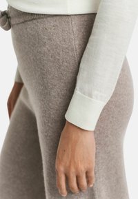 Haut à manches longues beige clair avec des poignets côtelés, associé à un pantalon tricoté marron clair avec une taille nouée et un discret logo.