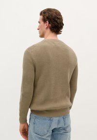 Ribbed knit, olive green sweater with a round neckline, fitted cuffs, and a straight hem, paired with light blue jeans.