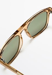 Bruna transparenta solglasögon med gröna linser; djärv rektangulär form, glansig finish, tunna metalldetaljer och distinkt bågdesign.