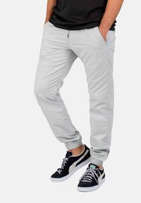 Pantalones jogger gris claro con puños elásticos, bolsillos laterales y una textura suave, combinados con zapatillas negras con detalles en gris.