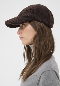Brown fleece baseball cap with a rounded crown, curved visor, and textured surface, worn at a slight angle, against a light background.