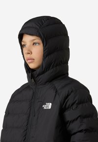 Μαύρο φουσκωτό μπουφάν με κουκούλα, χαρακτηριζόμενο από υφή με ραφές και εμπρόσθιο  φερμουάρ. Το λογότυπο The North Face εμφανίζεται στο πάνω αριστερό μέρος του στήθους.