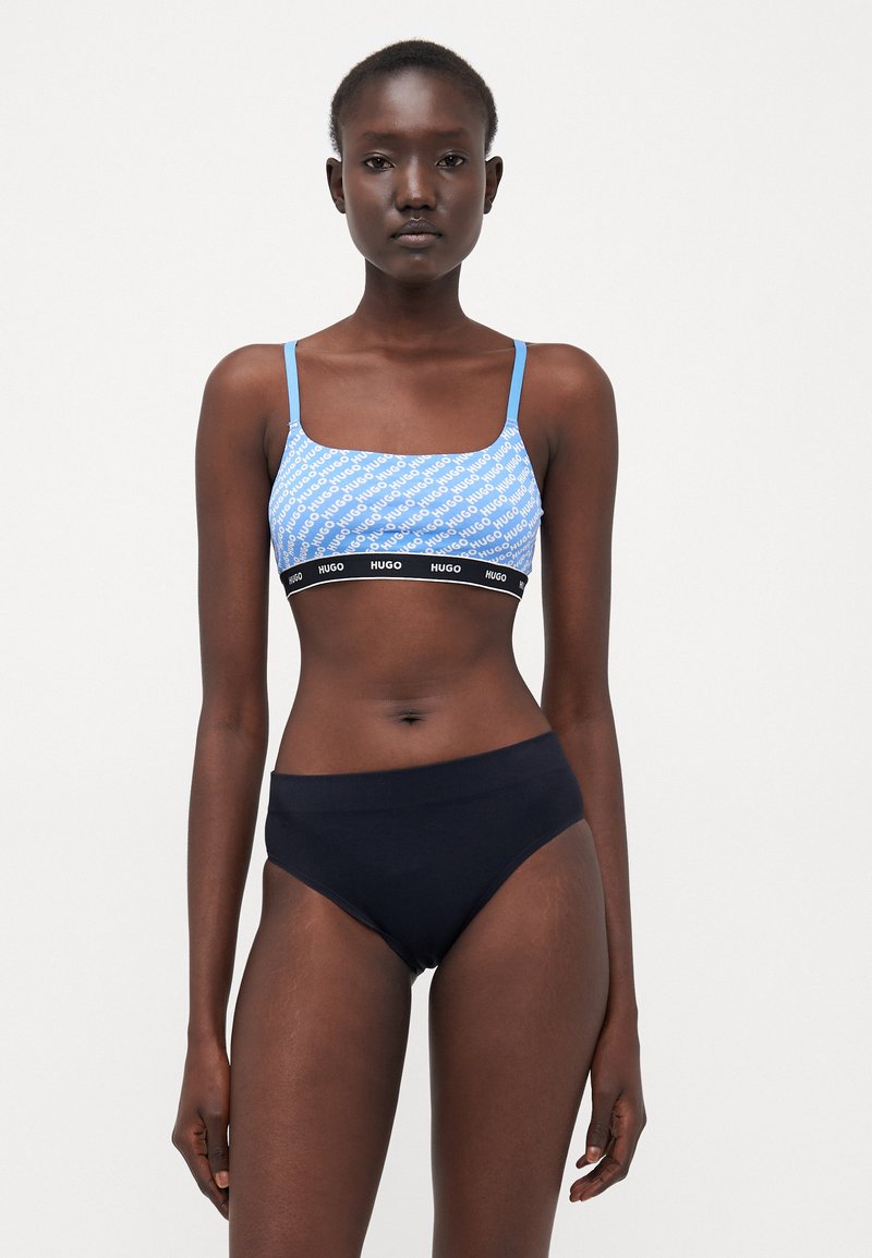 Blue patterned bralette with thin straps, black elastic band featuring the brand name, paired with solid black high-waisted underwear.