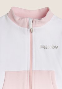Chaqueta blanca con cremallera, cuello y bolsillo rosas. Cuenta con el logo plateado "FREDY", material de algodón suave y un panel de color contrastante.