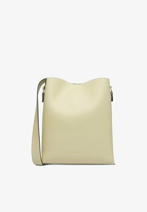 Krémově zbarvená hladká kožená kabelka přes rameno se širokým popruhem a decentním zlatým logem uprostřed přední strany.