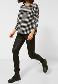 Black and white checked long-sleeve top paired with fitted black leggings and black lace-up ankle boots, featuring rolled cuffs.