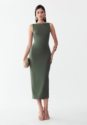 Frau in einem figurbetonten ärmellosen Midi-Kleid in Olivgrün, die eine geflochtene Clutch hält, trägt goldene Ohrringe, ein Armband und Riemchen-Sandaletten mit hohem Absatz.