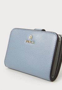 Portafoglio in pelle blu chiaro con finitura texture, dettaglio del logo dorato "FURLA" e rifiniture nere. Forma rettangolare compatta con chiusura a scatto.