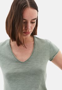 T-shirt verde chiaro a collo a V con maniche corte, caratterizzato da una consistenza morbida e un delicato motivo melange. Il collo è ben definito.