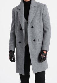 Dvoupřadový šedý vlněný kabát s klopovým límcem, černými knoflíky a bočními kapsami, doplněný šedou vestou a černými rukavicemi.