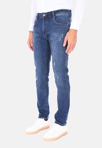 Jeans in denim blu slim fit con vita a media altezza, leggeri segni di usura e design a cinque tasche, abbinati a sneakers bianche.