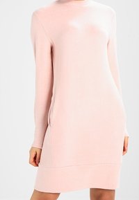 Abito a maglia rosa chiaro con maniche lunghe, scollatura rotonda e tasche laterali. Il tessuto sembra morbido e con una superficie liscia.