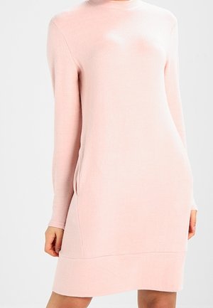 Robe tricotée rose pâle avec des manches longues, un col rond et des poches latérales. Le tissu semble doux avec une texture lisse.