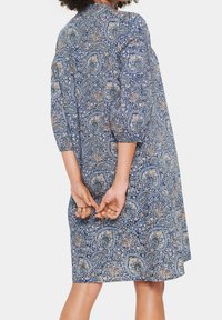 Blå klänning med paisleymönster, trekvartsärmar, rund halsringning och avslappnad passform, med intrikata mönster i kräm- och orangetoner.