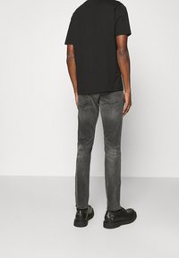T-shirt nera abbinata a jeans grigi sbiaditi e scarpe nere. La maglietta ha un collo rotondo e maniche corte; i jeans presentano un design aderente.