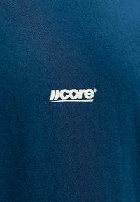 Camiseta de algodón azul marino con un logo blanco que dice "jjcore", tela texturizada con un acabado suave.